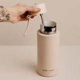Person holding a beige water bottle with a silver cap and white lid on a beige background