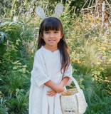 Young girl in a garden wearing bunny ears and holding a basket.