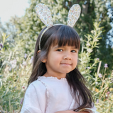 Young girl wearing floral bunny ears outdoors with greenery in the background