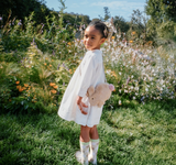 Young girl in a white dress holding a teddy bear in a field of flowers