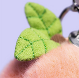 Green leaf-shaped keychain held by a hand against a light purple background