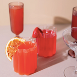 Red drinks in clear glasses on a light surface with an orange slice.