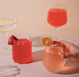 Two glasses of red and pink drinks with garnishes on a light surface.