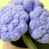Pair of purple fuzzy slippers with rhinestone embellishments on a green surface.