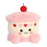 Plush toy shaped like a cake with pink frosting, red cherry, and heart decorations on a white background.