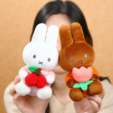 Two plush toys, one white and one brown, held by a person against a beige background.