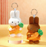 Two plush keychains shaped like bunnies holding carrots on a beige background