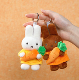 Two plush keychains shaped like a rabbit and a rabbit with a carrot, held against an orange background.
