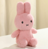 Pink plush bunny toy on a white surface with a beige curtain background