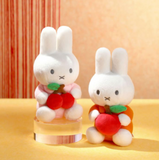 Two plush toys resembling bunnies with red apples on a yellow surface.