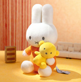 Plush toy rabbit wearing an orange outfit with a yellow chick on a yellow floor.
