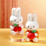 Two plush toys resembling bunnies with red apples on a yellow surface.