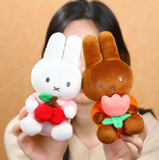 Two plush toys, one white and one brown, held by a person against a beige background.