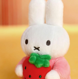 White plush toy rabbit holding a red strawberry with a green leaf on a yellow background