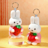 Two plush keychains of a white rabbit holding a strawberry on a beige background