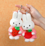Two plush keychains shaped like bunnies holding strawberries, held by a hand against an orange background.