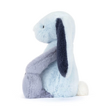 A light blue plush bunny toy sitting down, featuring dark navy blue floppy ears, a lavender-gray front paw, and a small white tail, photographed on a seamless white background.