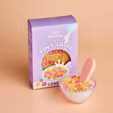 Box of 'tiny harlow' Tiny Loops cereal with a bowl of cereal and pink spoon on a beige background