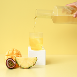Person pouring a drink into a glass with fruits on a yellow background