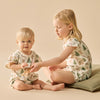 Two children in matching pajamas sitting on a beige surface.