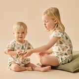 Two children in matching pajamas sitting on a beige surface.