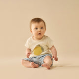 Baby wearing a white shirt with a yellow design and denim shorts on a beige background