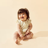 Baby sitting on a beige background wearing a lace romper.