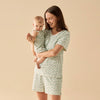 Woman and child wearing matching green floral outfits against a beige background