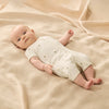 Baby lying on a beige blanket wearing a white outfit with small patterns.