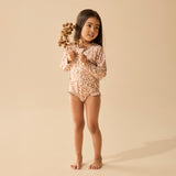 Young girl in a floral swimsuit holding dried flowers against a beige background