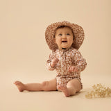 Baby wearing a floral sunsuit and hat on a beige background