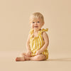 Baby wearing a yellow striped romper sitting on a beige background