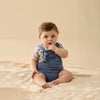 Baby wearing a blue romper with a beige background
