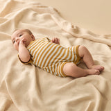 Baby wearing a yellow and white striped onesie lying on a beige blanket