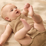 Baby in a beige knitted outfit lying on a soft surface