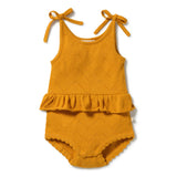 A baby romper in a warm mustard yellow color, featuring a textured eyelet knit pattern, ruffled hem, and tie-shoulder straps, shown flat on a white background.