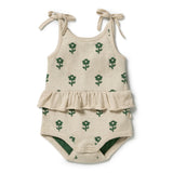 A baby romper in a light beige linen-like fabric with a green floral pattern, featuring thin shoulder ties and a ruffled hem, shown on a plain white background.