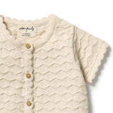 Close-up of a cream-colored short-sleeve baby cardigan with a wavy textured knit pattern, scalloped edges, and wooden buttons, shown on a white background.