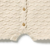 Close-up of a cream-colored textured knit baby romper with scalloped edges and wooden snap buttons, shown on a white background.
