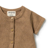 A close-up of a short-sleeve knit baby top in warm tan brown, featuring a button-down front with wooden buttons and a visible neck label reading 'woven & friendly'.