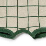 Close-up of a knit garment, likely a baby bodysuit or sweater, featuring a cream base with a dark green windowpane grid pattern and matching green ribbed trim.