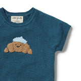 A close-up of a teal blue knit short-sleeve top featuring a croissant applique with a light blue hat on the chest. The brand label reads 'waffle waffle'.