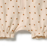 Close-up of a cream-colored ribbed baby romper with a small brown and black ladybug pattern, featuring a ruffled leg opening and a zipper at the chest.