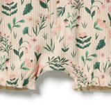 Close-up of a cream-colored ribbed romper with a green and pink floral print, featuring ruffled leg hems.