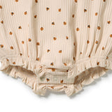 Close-up of a cream-colored ribbed fabric garment with a small brown and orange floral pattern, featuring elasticized ruffled trim and snap closures at the bottom.