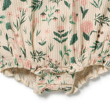 Close-up of a baby romper or bodysuit fabric with a cream base, featuring a green and pink floral print and ruffled trim at the bottom.