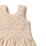 Close-up of a sleeveless baby dress in a warm beige/cream color with a small brown and black floral pattern, featuring a smocked bodice and gathered skirt.