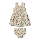 A baby girl's two-piece outfit set consisting of a sleeveless smocked dress and matching diaper cover, both featuring a green and pink floral print on a cream-colored textured fabric, shown on a plain white background.