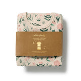 A folded organic cotton sleepwear set wrapped in a brown paper band, featuring a light beige ribbed fabric with a green leaf and pink floral pattern.