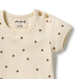 A close-up of a cream-colored ribbed short-sleeve baby top with small brown clover motifs and two wooden buttons on the shoulder, by nature friendly.